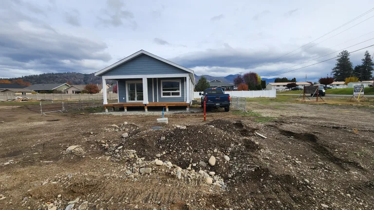 A modular home with Hardie Plank siding and covered front porch under construction in the West Grand Forks subdivision, with a truck and utility lines visible.